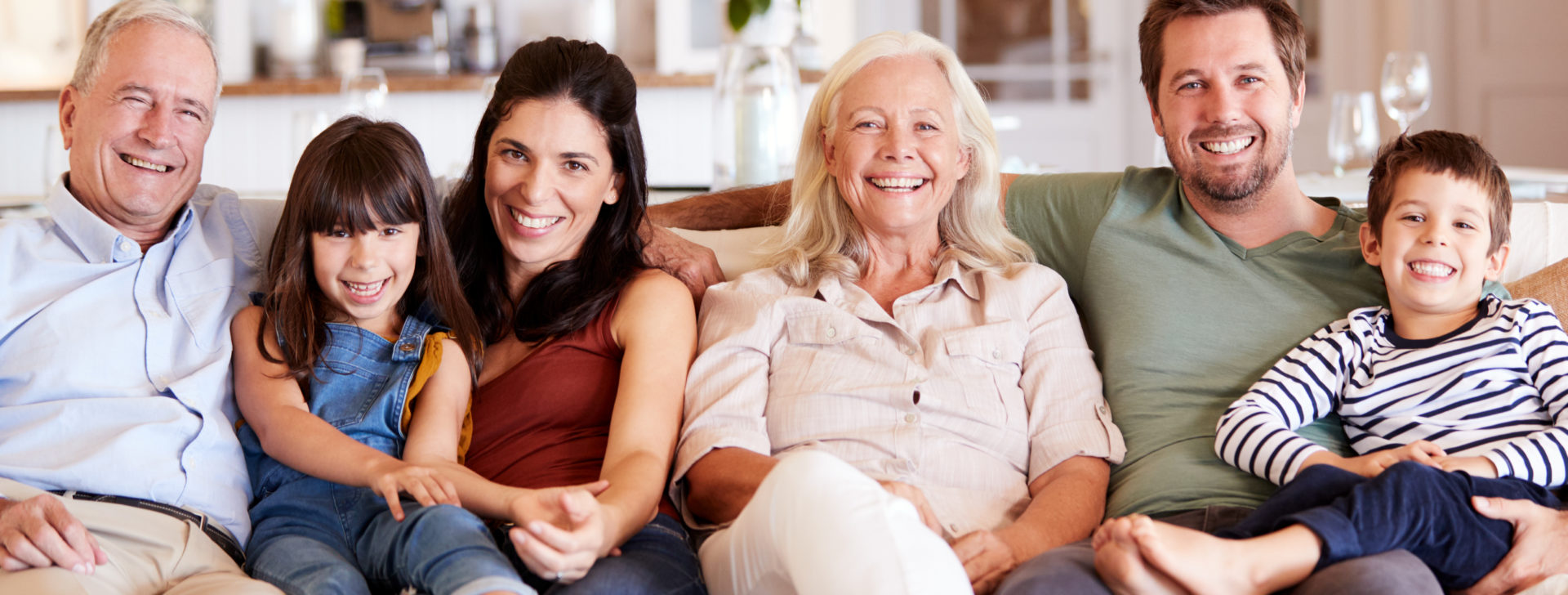 Happy three generation white family sitting on a sofa together at home smiling to camera, front view